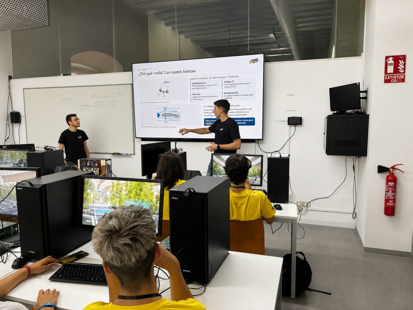 Dos miembros del equipo dando la clase de teoría ante la pantalla de las cuatro fuerzas del vuelo, con los chavales del campamento en los puestos de simulador