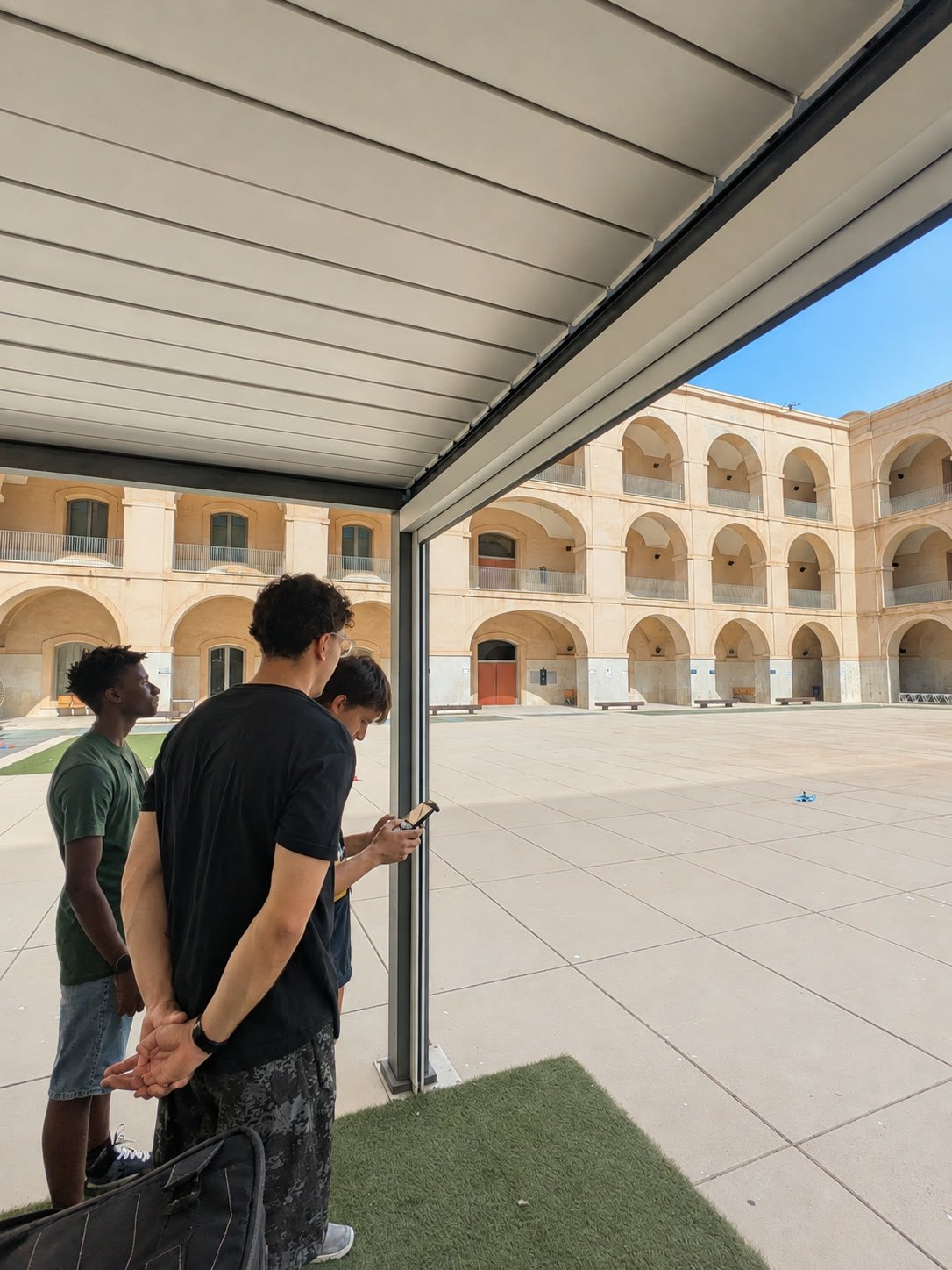 Tres chavales siguiendo el vuelo del dron en el patio durante los vuelos supervisados